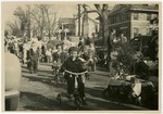 Parade scene with a decorated Christmas tree in a wagon and children on tricycles and walking