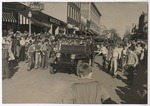 Parade scene with children following a Jeep to get candy that is thrown from the Jeep